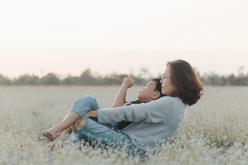 Mother hugging her son while relaxing together in beautiful flower field nature park during sunset. Love, care, happiness  Motherhood, family lifestyle, affection, childhood fun, summer, Mother’s Day.