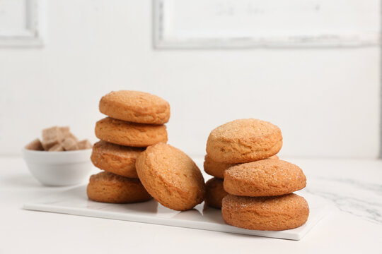 Board with sweet cookies and bowl of sugar on white background