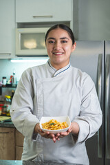 Smiling chef holding plate of pasta in kitchen