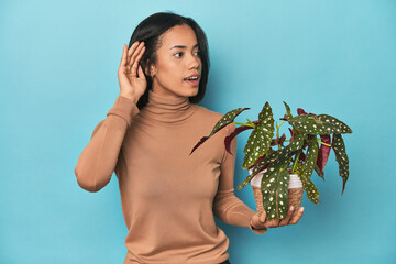 Filipina holding a plant on blue studio trying to listening a gossip.