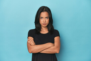 Filipina young woman on blue studio frowning face in displeasure, keeps arms folded.