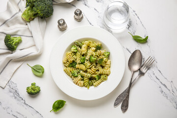 Plate of delicious fusilli pasta with broccoli and glass of water on white background