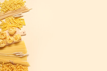 Composition with different types of raw pasta, wooden cutting board and wheat spikelets on beige...