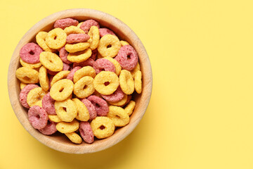 Wooden bowl with color cereal rings on yellow background, closeup