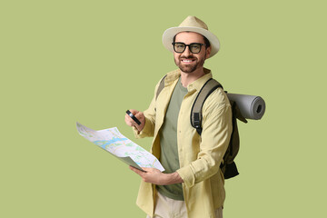 Young male tourist with magnifying glass and map on green background