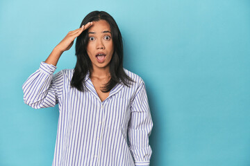 Filipina young woman on blue studio shouts loud, keeps eyes opened and hands tense.