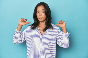 Filipina young woman on blue studio feels proud and self confident, example to follow.