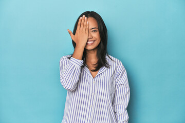 Filipina young woman on blue studio having fun covering half of face with palm.