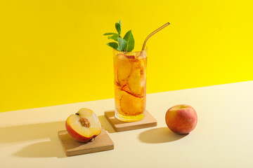 Glass of tasty iced tea with mint and peaches on beige table against yellow background