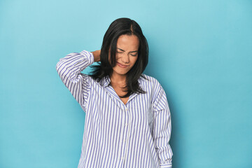 Filipina young woman on blue studio suffering neck pain due to sedentary lifestyle.
