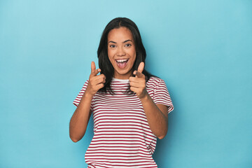 Filipina young woman on blue studio pointing to front with fingers.