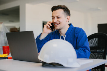 Smiling engineer working on laptop and talking on mobile phone