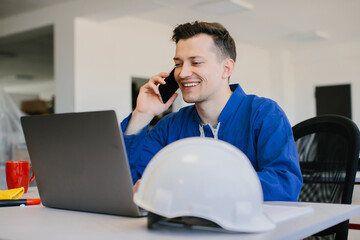 Smiling engineer talking on phone and working on laptop