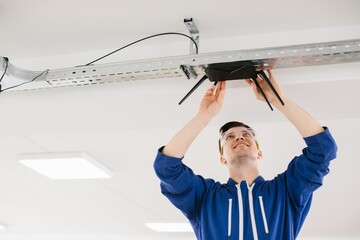 Technician installing wireless router on ceiling in office building