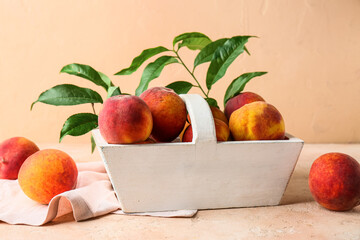White basket with sweet ripe peaches and leaves on beige background