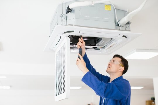 Hvac technician repairing air conditioner unit using screwdriver