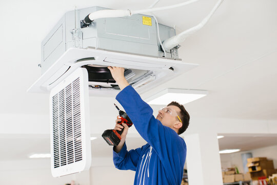 Hvac technician installing air conditioner unit using electric drill