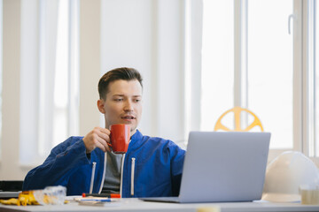 Young worker drinking coffee and using laptop in office