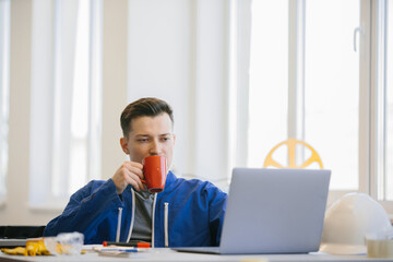 Worker drinking coffee and using laptop in office
