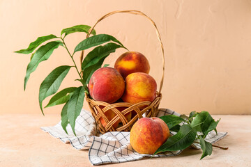 Wicker basket with sweet ripe peaches and leaves on beige background