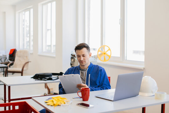 Focused factory worker checking inventory using clipboard and laptop