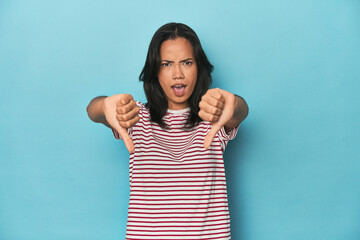 Filipina young woman on blue studio showing thumb down and expressing dislike.