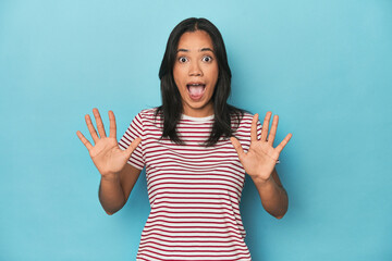 Filipina young woman on blue studio receiving a pleasant surprise, excited and raising hands.