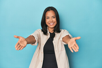 Filipina young woman on blue studio showing a welcome expression.