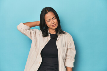 Filipina young woman on blue studio suffering neck pain due to sedentary lifestyle.