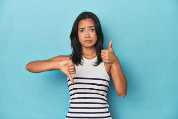 Filipina young woman on blue studio showing thumbs up and thumbs down, difficult choose concept