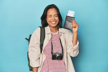 Filipina traveler displaying flight ticket with camera and backpack on blue