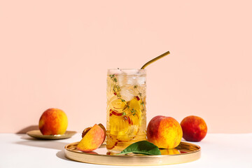 Glass of fresh peach lemonade with thyme and fruits on white table against beige background