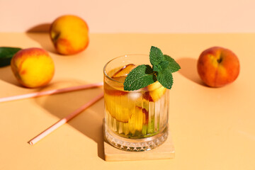 Glass of fresh peach lemonade with mint and fruits on orange table against beige background