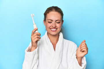Blonde in bathrobe with electric toothbrush in studio screaming very angry and aggressive.