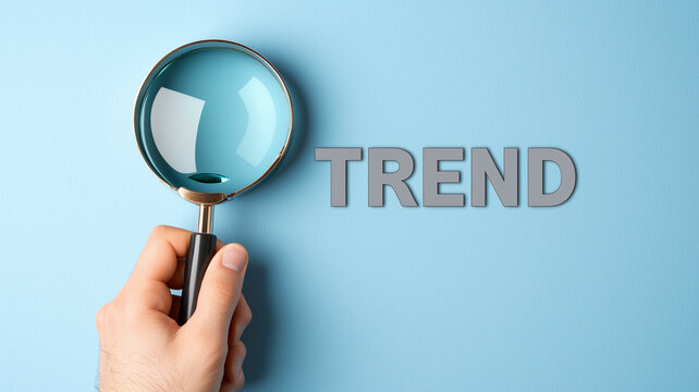 Trend Analysis Concept with Hand Holding a Magnifying Glass Over the Word TREND on Pastel Wall.
