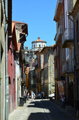 Fototapeta premium Narrow cobblestone street in Porto, Portugal, lined with colorful historic buildings and crowned by the iconic Serra do Pilar Monastery under a clear blue sky