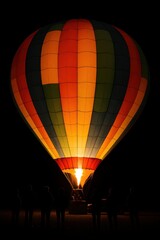 Obraz premium Colorful hot air balloon at night with silhouetted onlookers