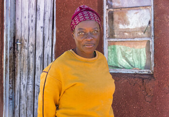 africa village, african woman in the township wearing a headscarf, cold day, standing outdoors in...