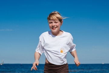 Blonde girl running on a sandy beach, enjoying a sunny summer day.