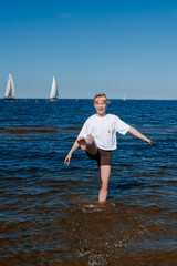 Blonde girl standing in the sea, striking a fun pose and smiling in the water.