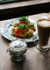 A plate of avocado toast sits on a wooden table next to a mug of coffee
