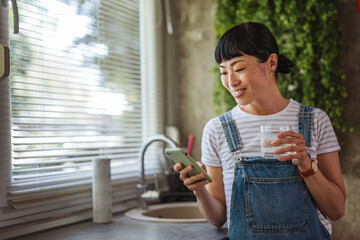 Japanese woman drink water and use mobile phone in the kitchen