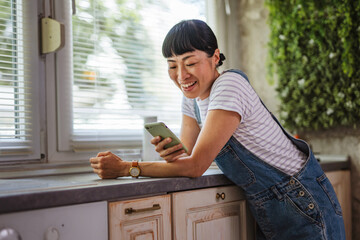 Japanese woman use mobile phone while stand in the kitchen