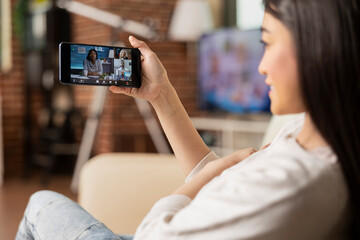 Businesswoman using cellphone, joins virtual shareholder meeting from apartment. Remote female...