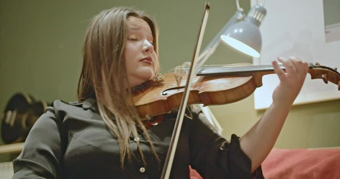 Young woman passionately playing the violin at home. She is practicing a beautiful melody and enjoys her hobby.