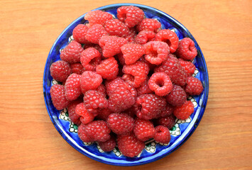 Ripe red raspberries on a blue plate on a wooden background. Sweet raspberry background. Berries close-up. Healthy food.