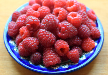 Ripe red raspberries on a blue plate on a wooden background. Sweet raspberry background. Berries close-up. Healthy food.