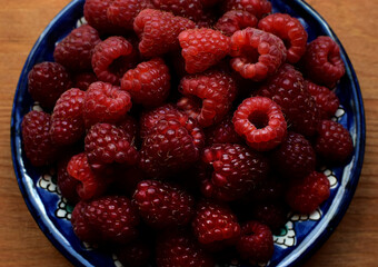 Ripe red raspberries on a blue plate on a wooden background. Sweet raspberry background. Berries close-up. Healthy food.