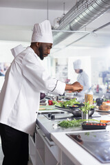 African american chef adding a sprinkle of rosemary to a gourmet dish on the stove, using fresh...