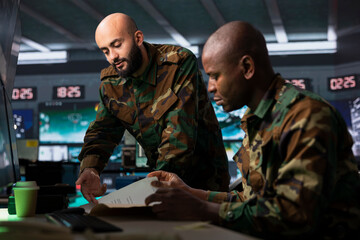 Team of military officers reviewing reconnaissance battlefield files to prepare field troops...